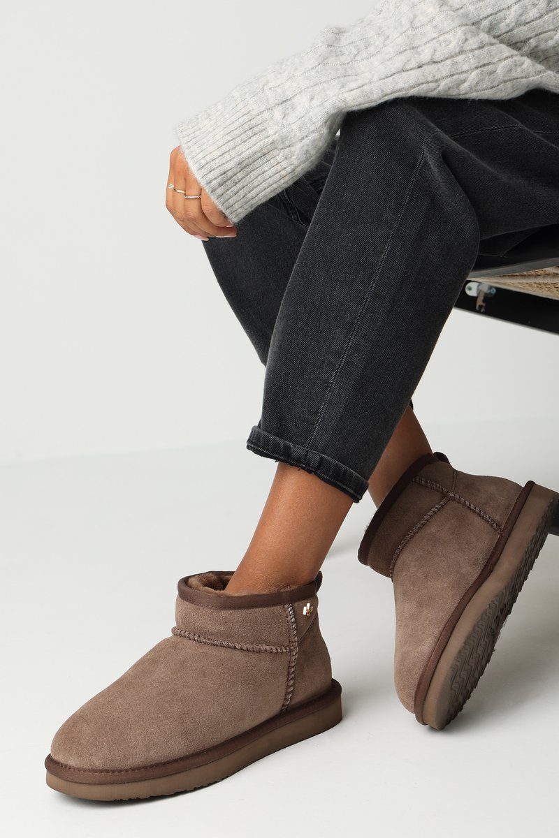 Botines de ante marrón con un suave forro interior, un diseño cosido y una suela de goma texturizada. Llevados con pantalones de mezclilla oscuros y enrollados.