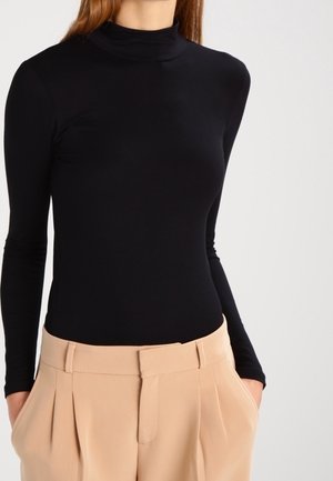 Sort langærmet rullekravetrøje med tætsiddende design, kombineret med beige bukser med høj talje, plisseringer og glat stoftekstur.