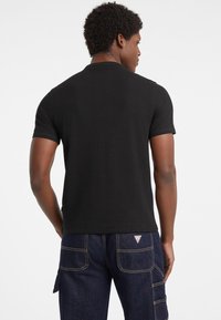 Czarna, prążkowana, krótko rękawowa koszulka polo z dopasowanym krojem, z klasycznym kołnierzykiem i subtelną teksturą, w połączeniu z ciemnoniebieskimi spodniami cargo.