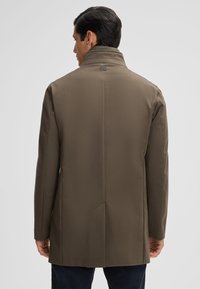 Bruine trenchcoat met een hoge kraag, een gladde textuur en een getailleerde pasvorm, met een enkele rugventilatie en een subtiele logo-detail op de hals.