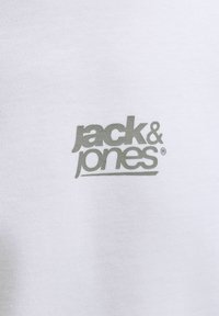 Λογότυπο "jack & jones" τυπωμένο σε γκρι πάνω σε λευκό πλεκτό ύφασμα.