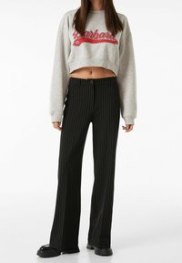 Grå kortärmad sweatshirt med röd text, tillsammans med svarta bredrandiga byxor med vida ben som har knappstängning och en mjuk yta.