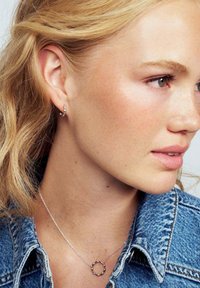 Silver hoops och cirkulär hängsmycke bärs med en denimjacka. Egenskaper inkluderar slät metalltextur och enkla cirkulära mönster.