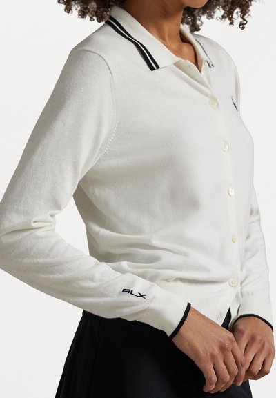 Valkoinen pitkähiha-polo-neule takki napilliseen etusulkeeseen, mustalla ribbikauluksella ja brodeeratulla "ALX"-logolla hihassa. Pehmeä, sileä pinta.