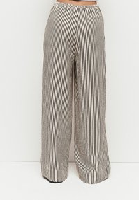 Stribede bredbenede bukser i beige og sort stof. Elastisk talje, løs pasform og lodrette striber, der skaber et tekstureret, flydende udseende.