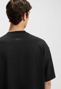 Black sweatshirt featuring a ribbed neckline and short sleeves, with a subtle "BOSS" logo printed on the upper back. Soft fabric texture.