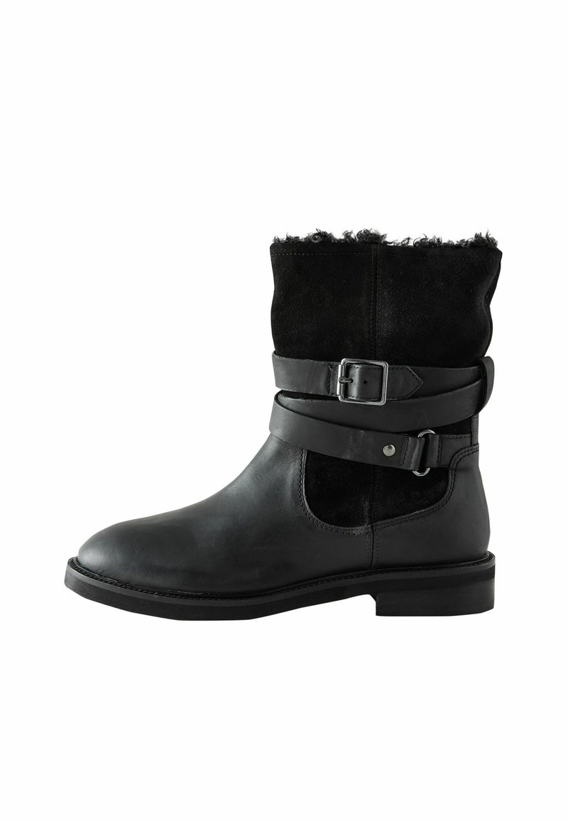 Stivaletto nero in pelle e camoscio, con una fascia con fibbia intorno alla caviglia, colletto in pelliccia testurizzata e tacco basso.