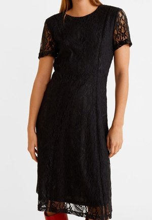 Czarna koronkowa sukienka do kolan z krótkimi rękawami, noszona przez osobę, prezentująca kwiatowe wzory koronki i dopasowaną sylwetkę.