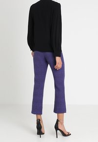 Blusa nera con maniche lunghe, abbinata a pantaloni con motivo a chevron viola. Sandali neri con tacco alto e dettaglio alla caviglia.