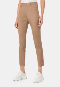 Světle hnědé strečové kalhoty se slim fit střihem, s pěti kapsami a klasickým zapínáním na knoflík, spárované s bílými sportovními teniskami.