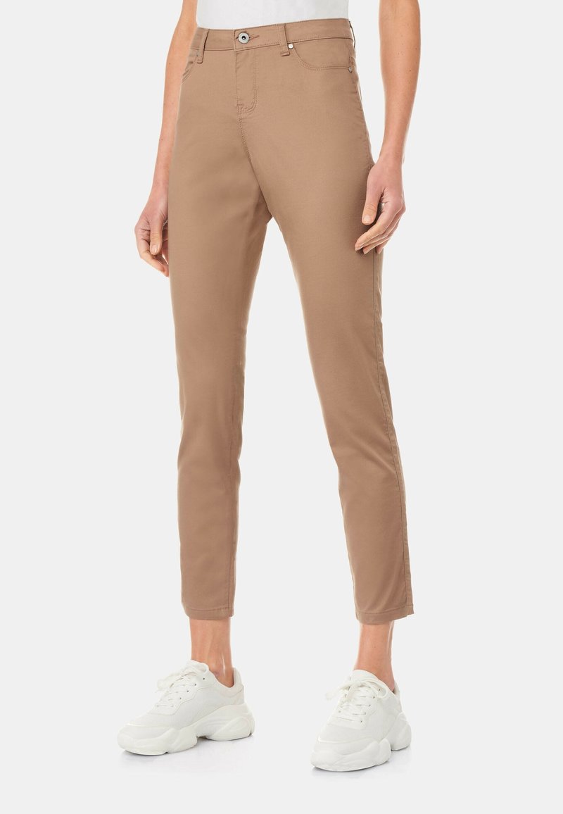 Světle hnědé strečové kalhoty se slim fit střihem, s pěti kapsami a klasickým zapínáním na knoflík, spárované s bílými sportovními teniskami.