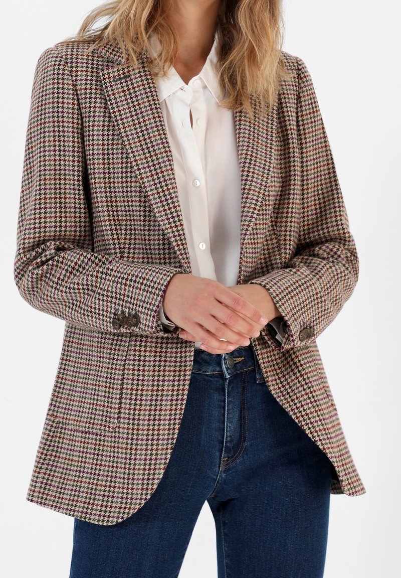 Rutig kavaj i bruna, krämiga och burgundy nyanser, tillverkad av texturerat tyg. Har slag med snitt och tvåknapps stängning. Kombineras med en vit skjorta.