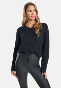 Schwarzer, flauschiger Strickpullover mit langen Ärmeln, V-Ausschnitt und lockerer Passform, kombiniert mit hoch taillierten, schwarzen Kunstlederhosen.