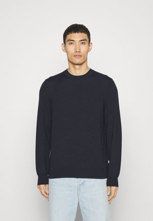 Marinefarbener Pullover mit langen Ärmeln und Rundhalsausschnitt, gerippten Bündchen und Saum; über hellblauen Jeans getragen. Glatte Textur, minimalistisches Design.