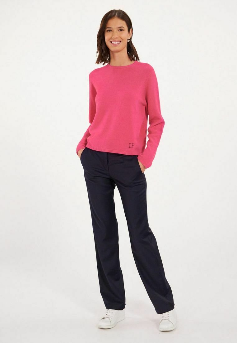 Pull en tricot fuchsia avec un col rond, associé à un pantalon bleu marine. Des baskets blanches complètent le look. Le pull est doté d'un détail brodé "IF".