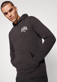 Hoodie noir avec une poche avant, arborant le logo "PUMA sports club" en blanc. Tissu texturé et capuche ajustable avec cordon.