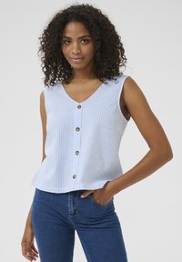 Haut sans manches rayé bleu et blanc avec un col en V et une fermeture à cinq boutons, fabriqué en tissu léger ; porté avec un jean bleu.