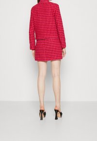 Set giacca e gonna con motivo a scacchi fucsia, caratterizzato da un taglio dritto, tessuto strutturato e mule nere con tacco, visto da dietro.