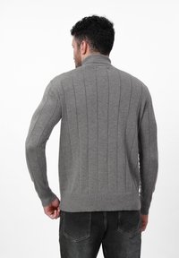 Grauer gerippter Strickpullover mit hohem Kragen, langen Ärmeln und taillierter Passform, getragen von einer Person, die von hinten vor einem weißen Hintergrund gezeigt wird.