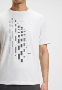 White cotton t-shirt featuring a graphic design in shades of gray with rectangular patterns, logo text "BOSS" in black at the bottom.
