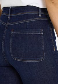 Jeans de tiro alto azul oscuro con costuras de contraste, que cuentan con un bolsillo trasero con un acento rojo. La tela vaquera tiene una textura suave.