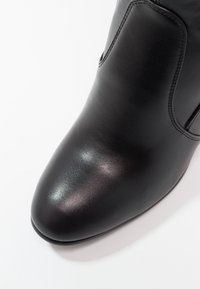 Botín negro de piel con puntera redondeada y textura suave, que presenta una costura a lo largo de los lados y un hardware minimalista.