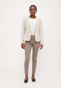 Beige skreddersydd blazer over en hvit skjorte, kombinert med lysebrune slim fit jeans og svarte leiligheter. Enkelt og strukturert design.