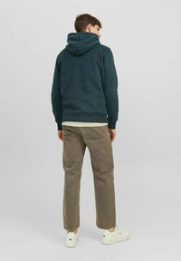 Sudadera verde oscura con capucha ajustable, combinada con una camiseta beige de capas y pantalones de pana marrón claro, usados con zapatillas blancas.