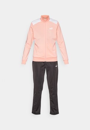 Růžová sportovní bunda na zip s bílými ramenními akcenty, v kombinaci s černými sportovními kalhotami. Vyrobena z měkké, hladké tkaniny s těsným střihem.