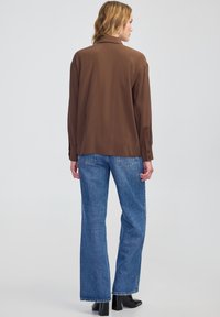 Brązowa koszula z długim rękawem i kołnierzykiem, w połączeniu z jasnoniebieskimi spodniami o szerokich nogawkach i czarnymi botkami za kostkę. Gładki materiał z luźnym krojem.