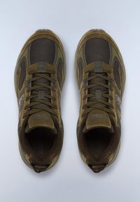 Zapatos deportivos marrones con un upper de cuero texturizado y gamuza, que presentan ojales reforzados, cordones oscuros en contraste y una suela de goma.