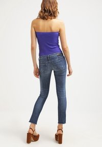 Top sin tirantes de canalé morado combinado con pantalones skinny de mezclilla azul desgastados. Los pantalones presentan detalles desgastados y dobladillo sin rematar. Sandalias de tacón de bloque de madera marrón.