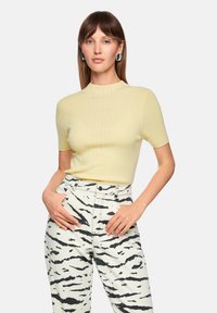 Light yellow ribbed short-sleeve top paired with white pants featuring black tiger stripe patterns. Plain round neckline and fitted design.