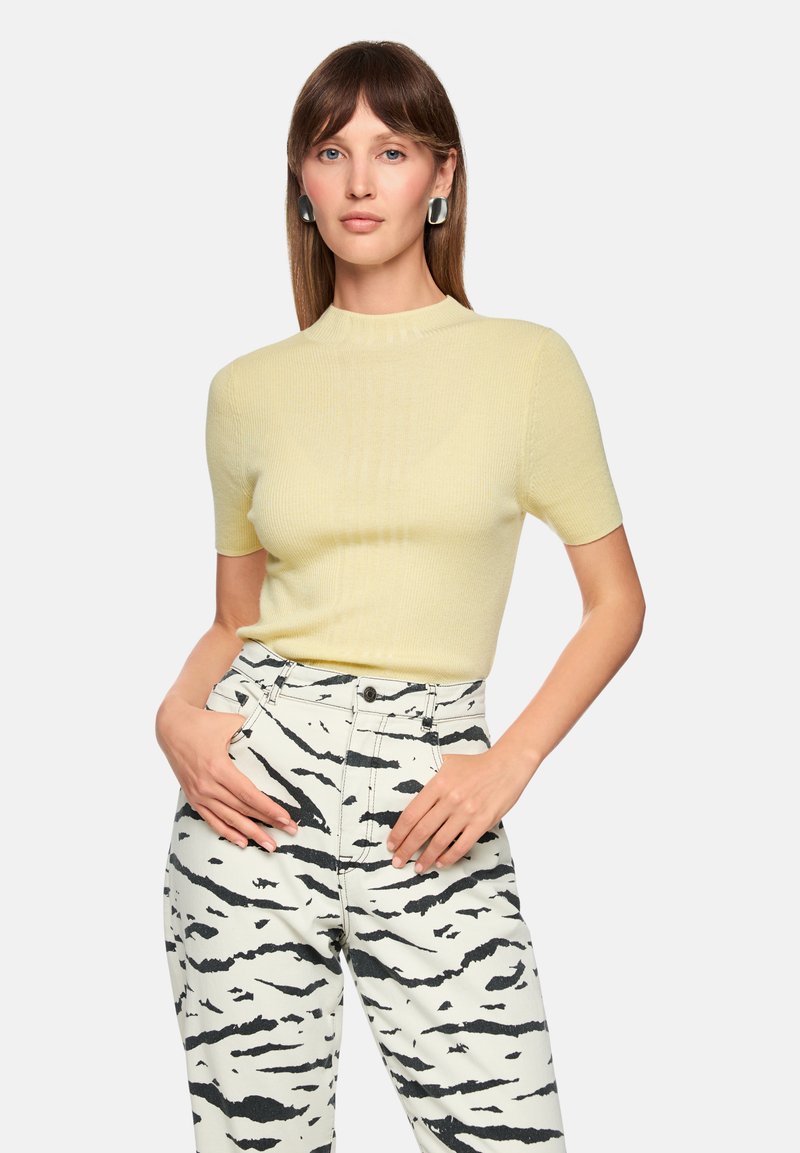 Light yellow ribbed short-sleeve top paired with white pants featuring black tiger stripe patterns. Plain round neckline and fitted design.