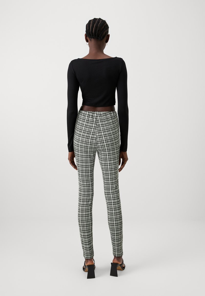 Svart långärmad croppad topp i kombination med gröna och svarta houndstooth-mönstrade tajta byxor. Modellen står med ryggen mot åskådaren.