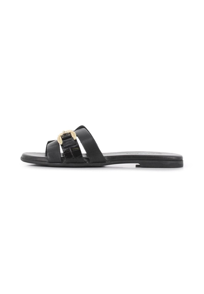 Sandalias planas negras con dos correas anchas, con un acento de hardware dorado. Fabricadas en cuero suave con un acabado mate y suela plana.