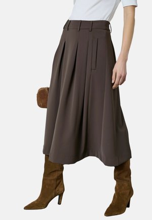Barna pliszírozott szoknya magas derekú kialakítással, sima anyagból készült, övbújtatókkal és oldalzsebekkel, magas barna velúr csizmával párosítva.