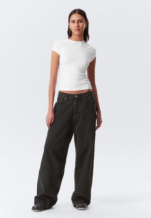 White ribbed short-sleeve top paired with loose-fitting, dark gray jeans. The jeans feature a button fly and front pockets, with a relaxed silhouette.