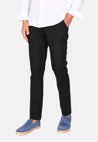 Schwarze Leinenhosen mit slim Fit, zwei Seitentaschen, kombiniert mit blauen Wildleder-Schlüpfschuhen und einem weißen Langarmshirt.