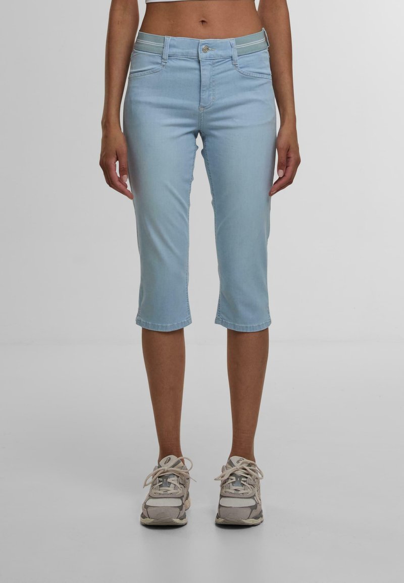 Lyseblå denim capribukser med en tettsittende midje, fem lommer og rullede nederkantar. Sammen med grå sneakers. Jevn tekstur.