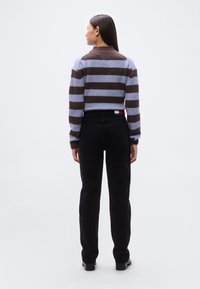 Κοντό πουλόβερ με οριζόντιες λωρίδες σε ανοιχτό μωβ και καφέ χρώμα· ριμπ υφή· συνδυασμένο με μαύρο τζιν παντελόνι ίσιας γραμμής και σκούρα υποδήματα.