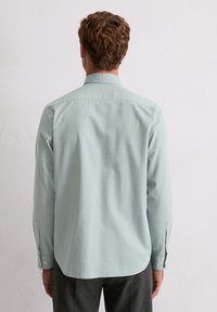Camicia a maniche lunghe verde chiaro con colletto a bottoni, morbida al tatto e dal taglio rilassato. Presenta polsini a bottoni e un orlo arrotondato.