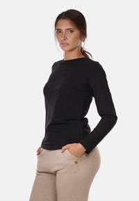 Maglietta nera a maniche lunghe realizzata in un tessuto morbido, con scollatura tonda. La camicia ha una vestibilità leggermente aderente ed è abbinata a pantaloni beige a trama.