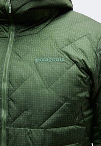Πράσινο καπιτονέ μπουφάν Patagonia με κουκούλα και φερμουάρ μπροστά, με διακριτικό μοτίβο πλέγματος και κεντημένο λογότυπο της μάρκας στο στήθος.