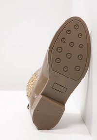 Suela de zapato beige con patrones circulares y agarre texturizado. Presenta una parte superior brillante. Talla marcada 36, etiquetado como "Hecho en Portugal."