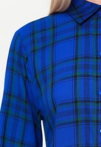 Blauwe geruite overhemden met een knoopsluiting aan de voorkant, voorzien van een kraag, een gestructureerde stof en meerkleurige patronen met groene en zwarte accenten.
