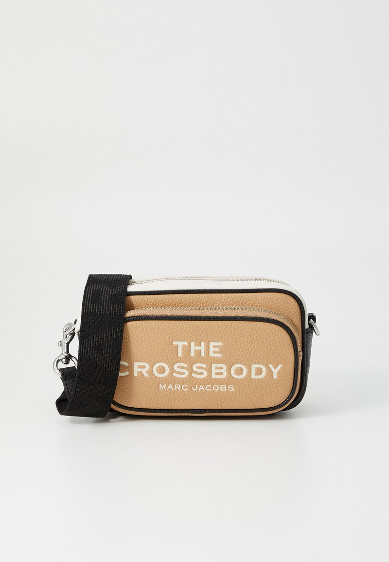 Tan leather crossbody bag with contrasting black accents, zip closure, adjustable strap, and white text on the front.