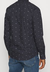 Camicia nera con un piccolo motivo geometrico in blu chiaro. Realizzata in tessuto dalla texture liscia, con maniche lunghe e chiusura con bottoni.