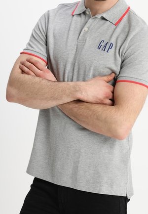 Polo gris avec des accents rouges sur le col et les manches, arborant un logo "GAP" bleu marine sur la poitrine. Fabriqué en tissu en coton mélangé texturé.