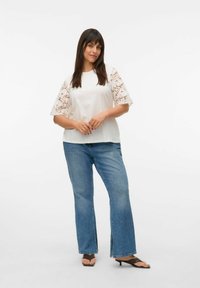 Witte top met kanten mouwen, gecombineerd met een paar blauwe flared jeans. Sandalen accentueren de outfit. Eenvoudig, schoon ontwerp met een losse pasvorm.